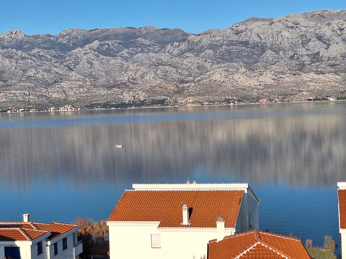 View across the calm Velebit channel toward the mountains, red-roofed houses by the shore